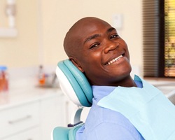 A young gentleman lying back in a dentist’s chair smiling while waiting for the dentist to arrive