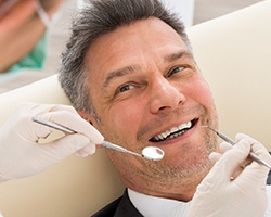 A middle-aged man lying on his back in the dentist’s chair while the holistic dentist in Weyauwega checks his smile