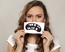 A woman holding a picture of an unhealthy smile over her mouth.