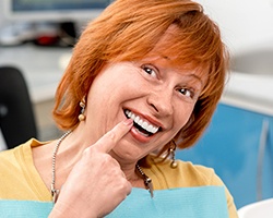 Senior woman in dental chair pointing to smile