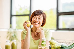 Smiling woman with dental implants in Weyauwega holding an apple