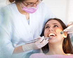A dentist using dental instruments to examine a female patient’s smile in preparation for mercury removal in Weyauwega