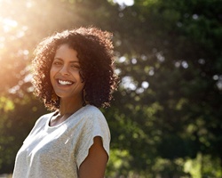 A middle-aged woman wearing a short-sleeved t-shirt and standing outside smiling after a successful recovery from having several teeth extracted