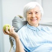 An older woman in the dentist chair holding an apple