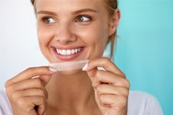 woman smiling while holding whitening strips