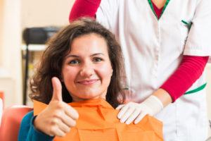Smiling woman in dental chair giving thumbs up