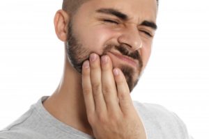 a younger man holding the side of his jaw and wincing in pain