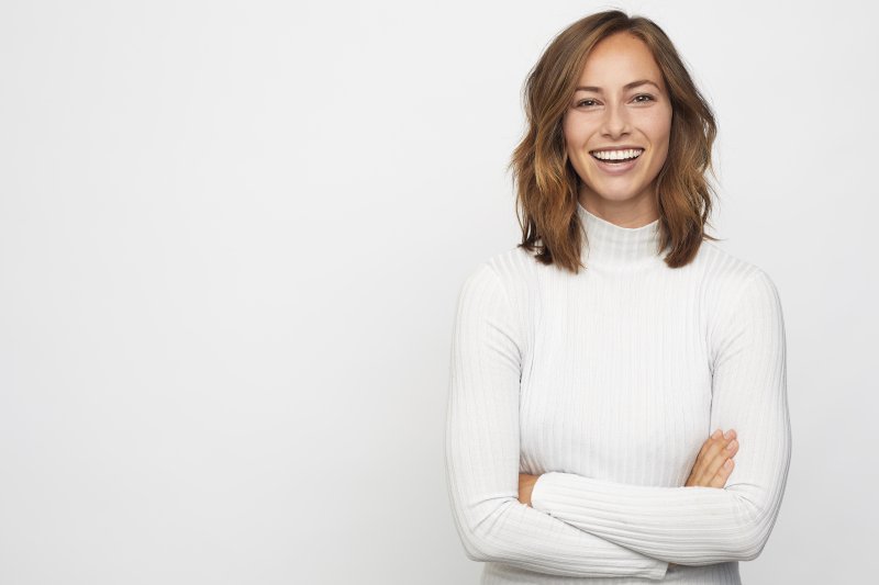 a young woman wearing a white turtleneck and smiling with her arms crossed in front of her