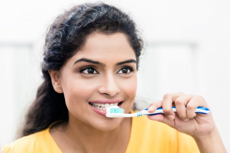 a young woman wearing a yellow blouse and brushing her teeth with a manual toothbrush