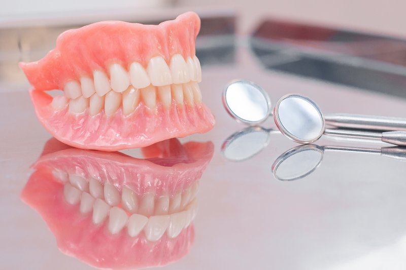 an upper and lower denture creating a full smile and sitting on a table next to two dental mirrors