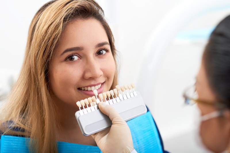 a dentist using a shade guide to determine the color of a female patient’s porcelain veneers